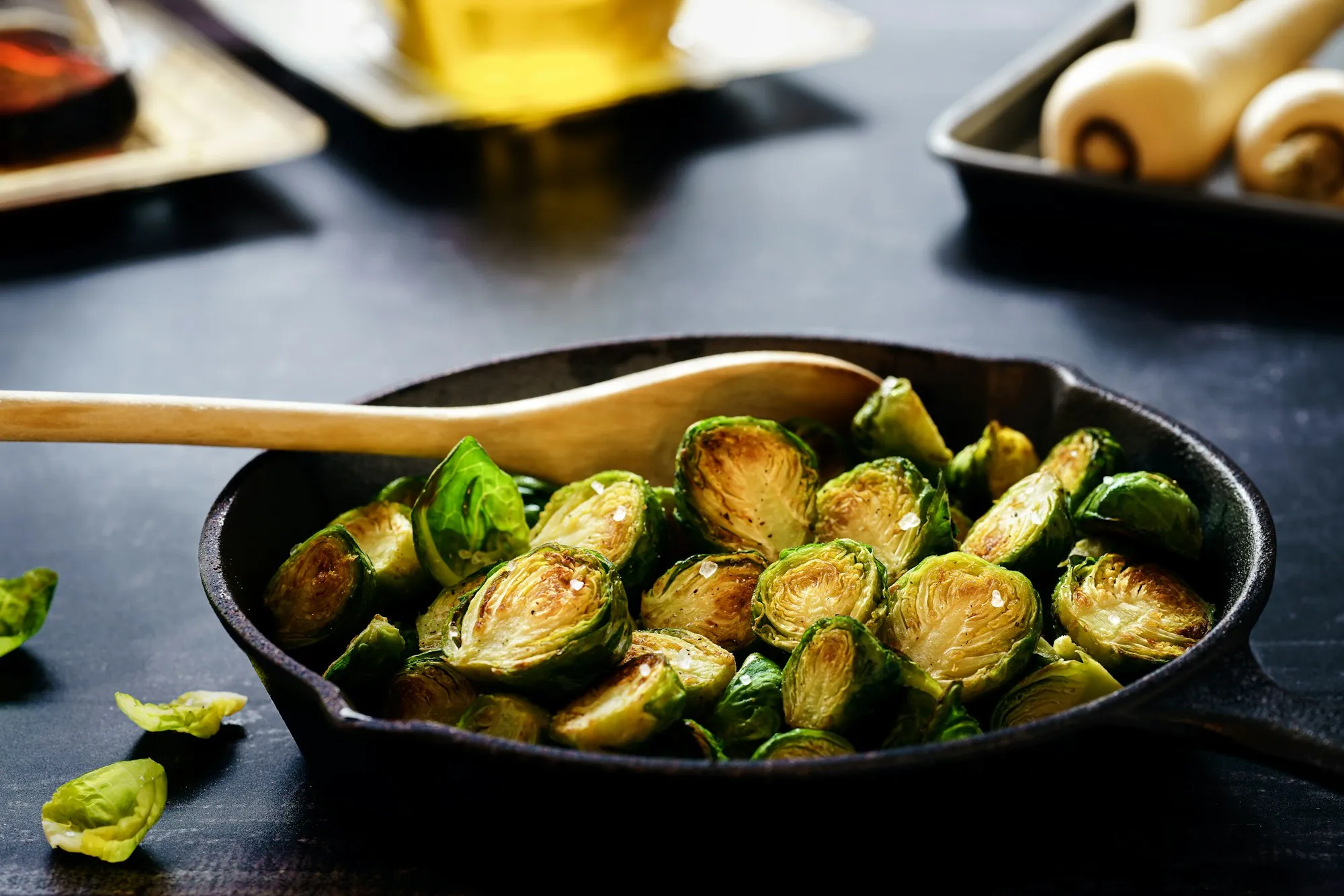 Caramelized roasted Brussels sprouts in a cast iron skillet with a wooden spoon (stock photo)