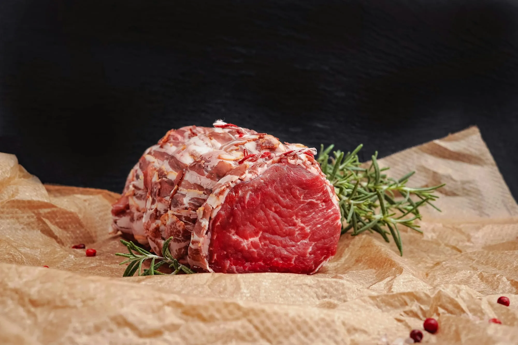 A tied raw beef roast with rosemary on butcher paper (stock photo)