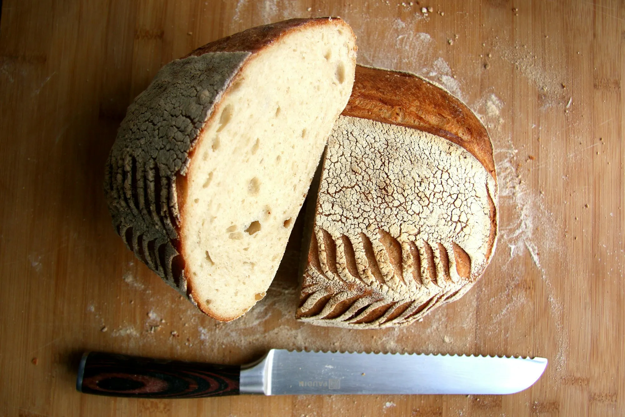 A flour-dusted country sourdough loaf cut in half beside a bread knife (stock photo)