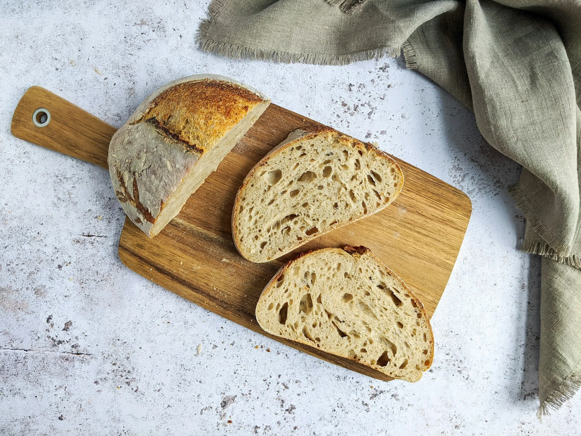 A crusty sourdough loaf cut into slices on a wooden board (stock photo)