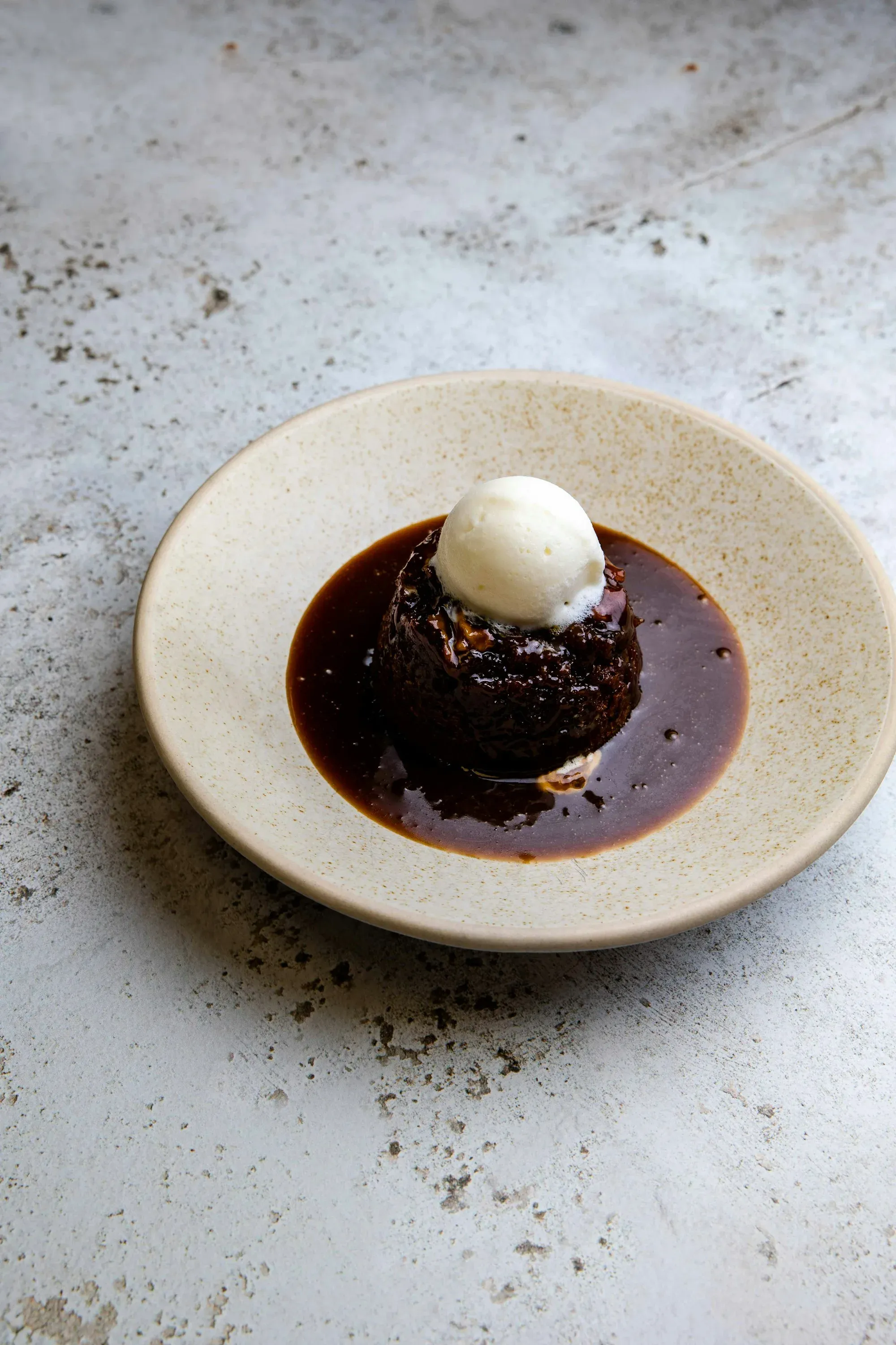 A small dark pudding in a pool of glossy sauce, topped with ice cream