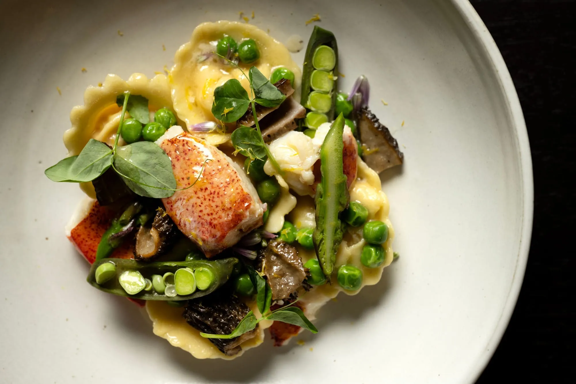 Ravioli with seared lobster, spring peas, morels and pea shoots in a white bowl