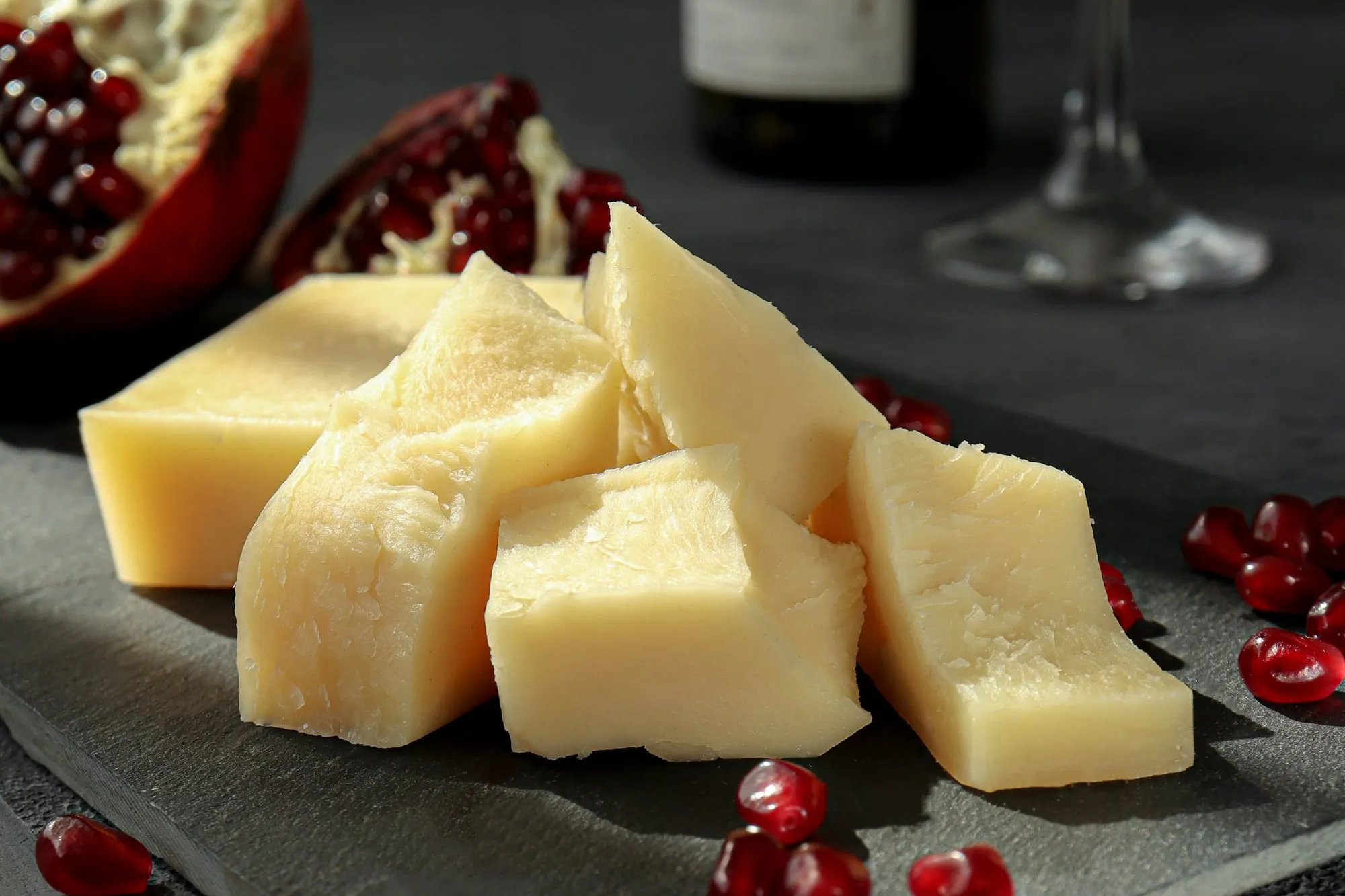 Chunks of aged cheese on a slate board with pomegranate seeds (stock photo)