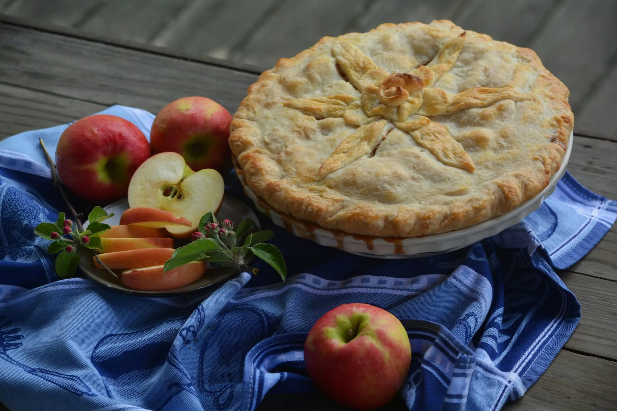 A golden double-crust apple pie beside fresh red apples and apple slices (stock photo)