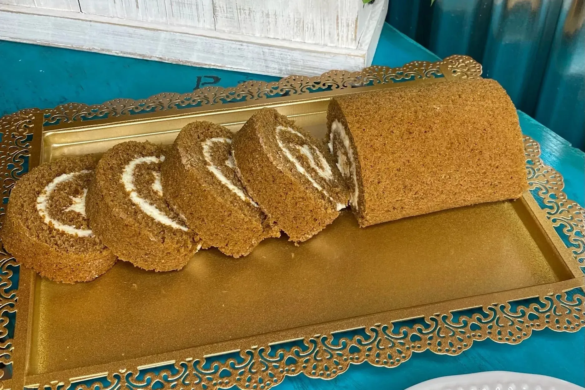 A sliced pumpkin roll with cream cheese swirl on a gold filigree tray