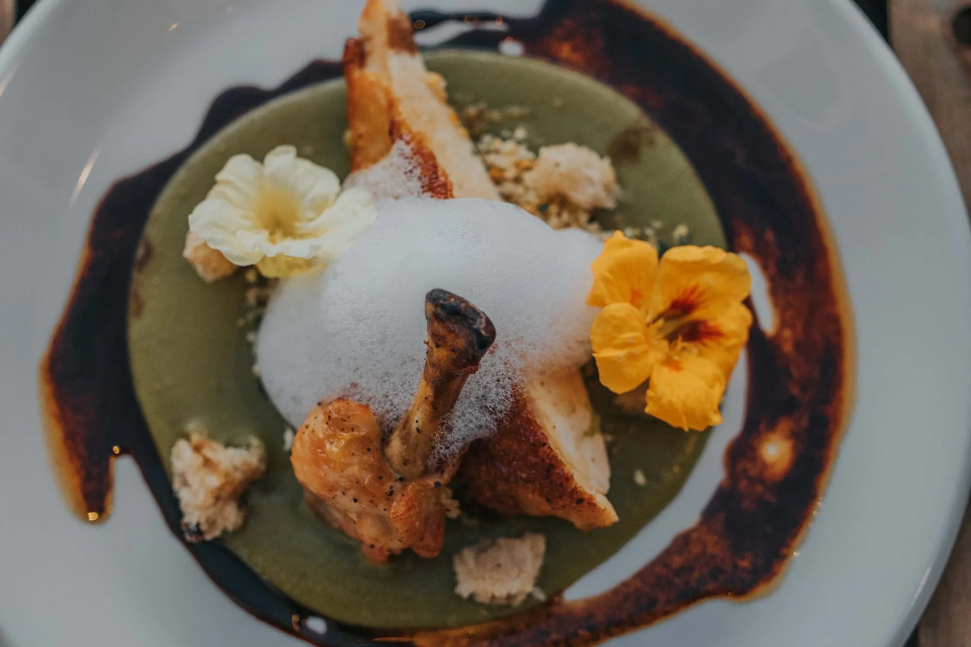 Roast heritage chicken with herb foam, a bright green sauce and nasturtium flowers on a white plate, from a farm dinner