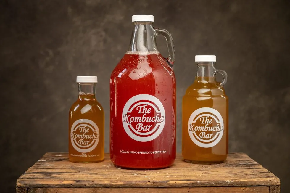 A growler of red kombucha between two smaller bottles of golden kombucha on a wooden crate