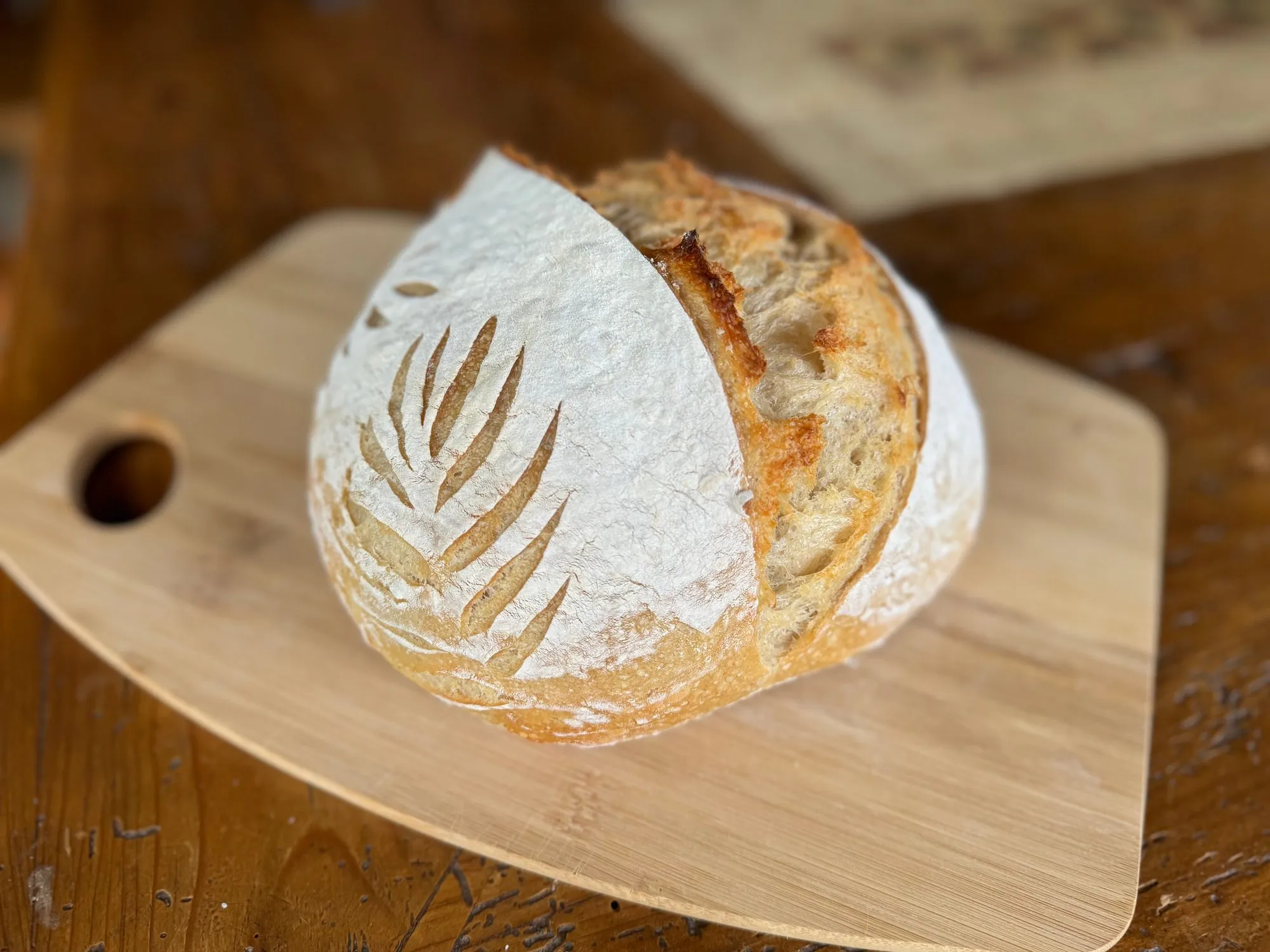 A flour-dusted sourdough boule with a wheat-stalk score on a wooden board