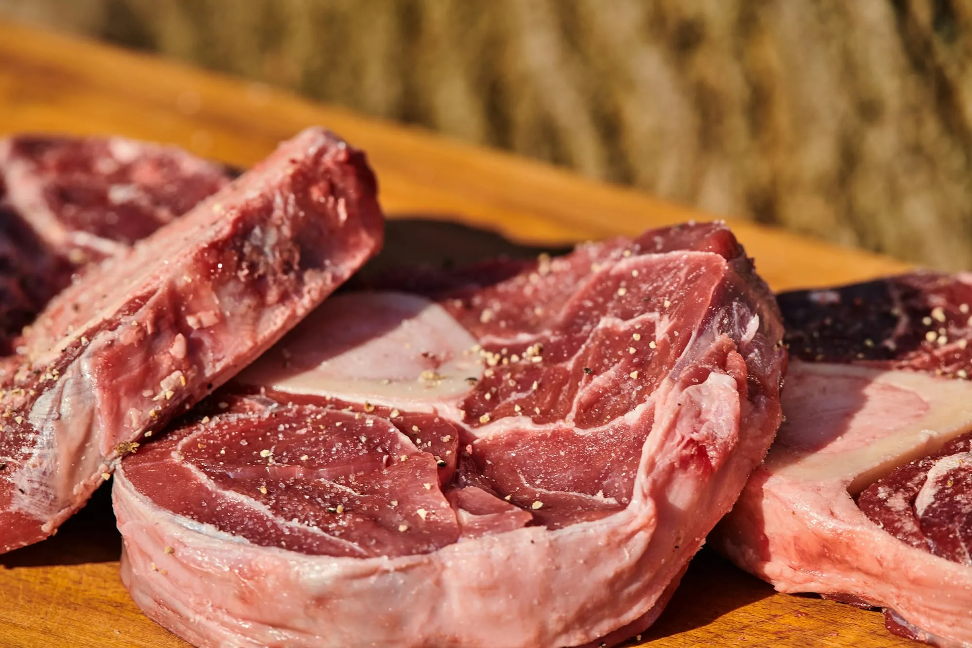 Thick raw bone-in beef steaks on a wooden board (stock photo)