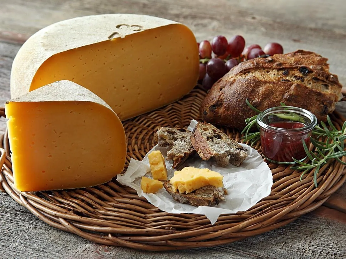Wheels of golden Califon Tomme cheese on a wicker tray with walnut bread, grapes and jam