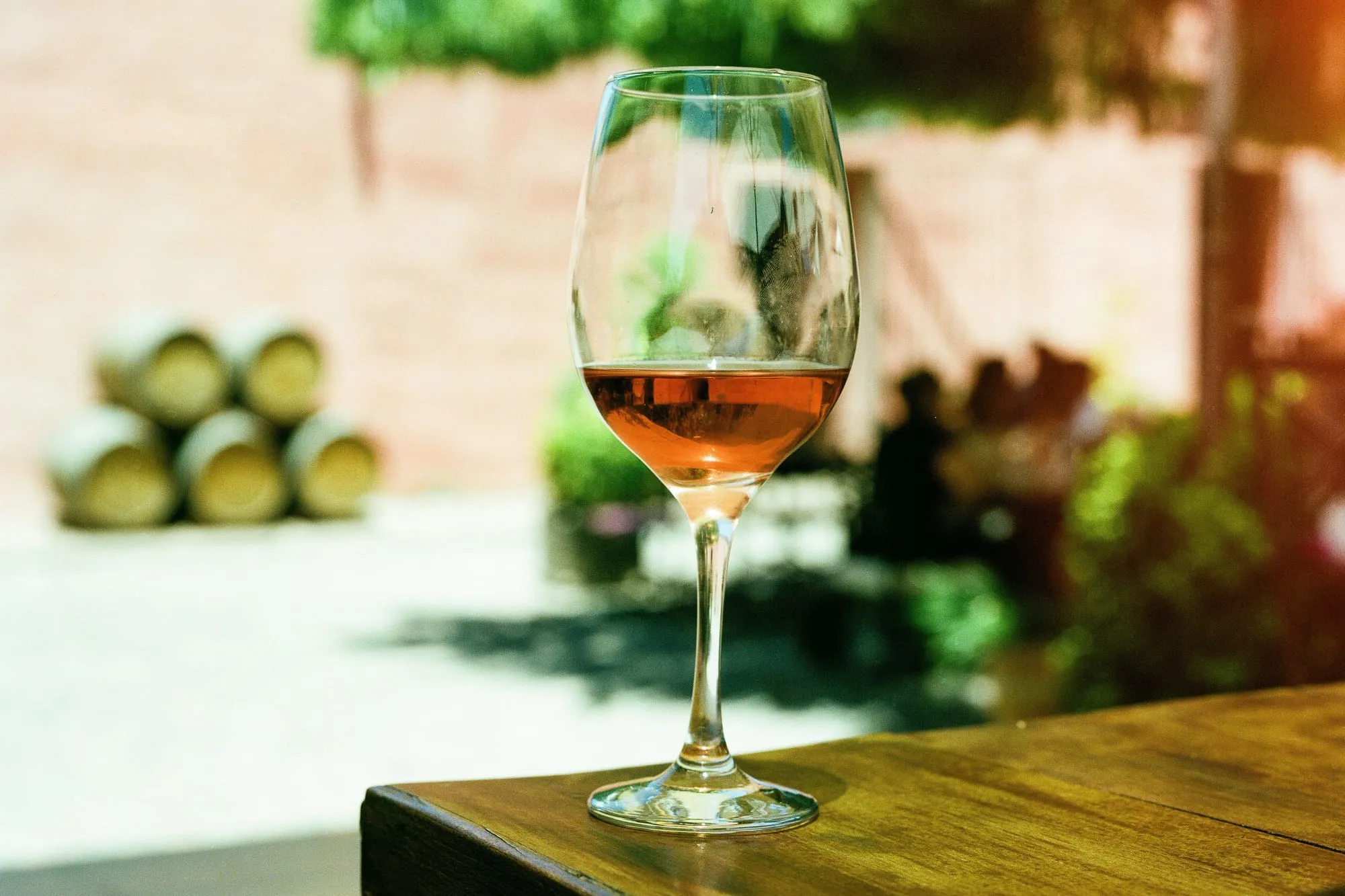 A glass of rose wine on a sunlit wooden table with oak barrels softly blurred behind (stock photo)