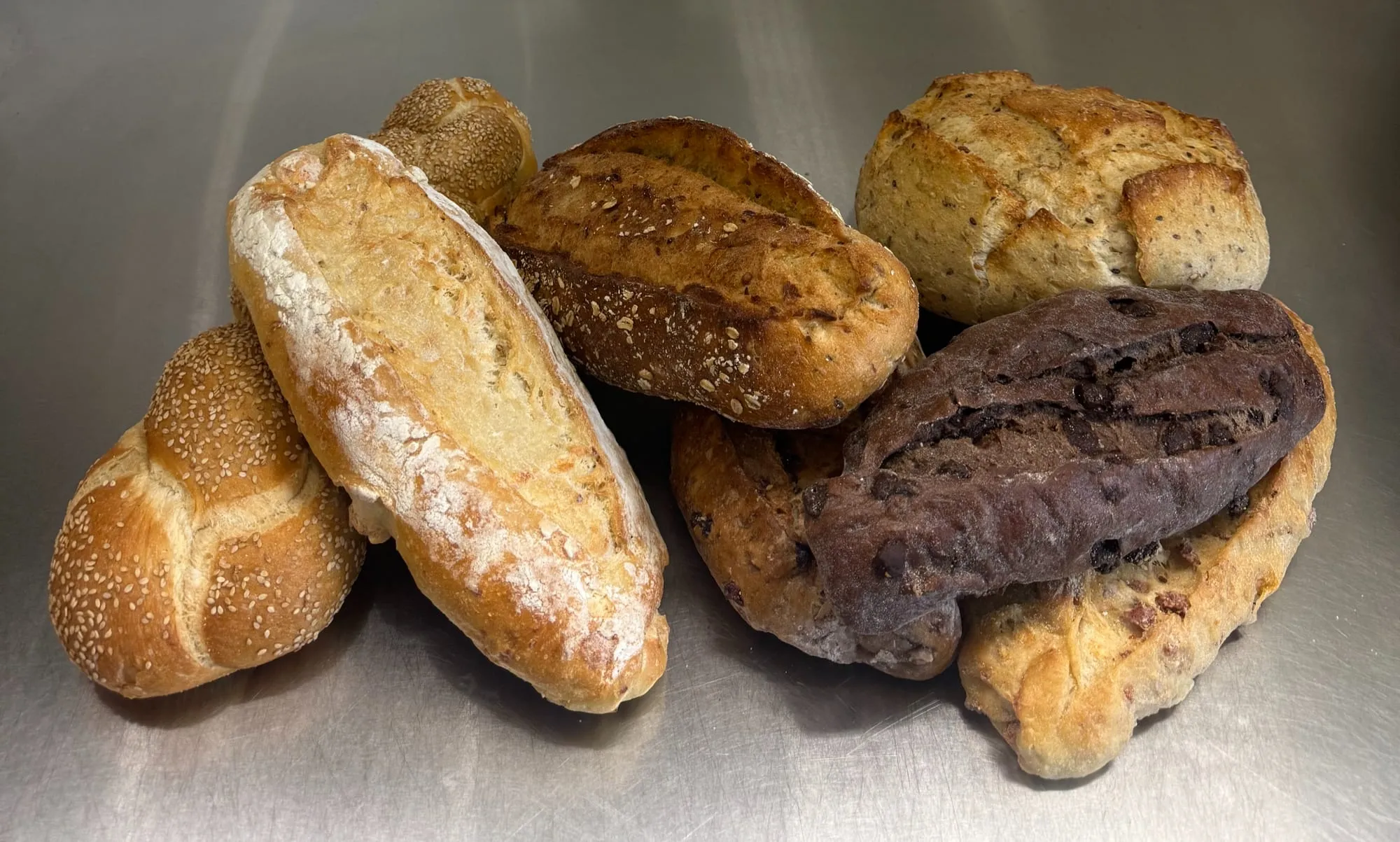 Assorted artisan loaves, including a semolina twist, a floury Italian loaf, a seeded batard and a chocolate loaf